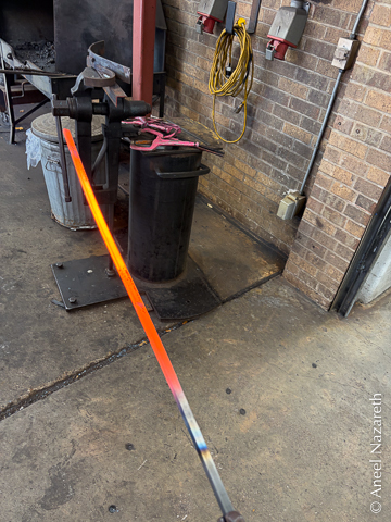 An orange-hot bar of steel is being carried over to the jig which is held in a vise